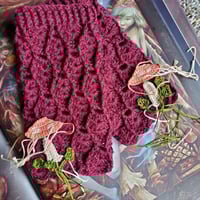 Photo shows a pair of unique handmade crochet fingerless cottagecore mittens with the makings of decorative crochet mushrooms and leaves in the process of being finished and added to the gloves.