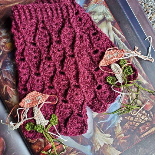 Photo shows a pair of unique handmade crochet fingerless cottagecore mittens with the makings of decorative crochet mushrooms and leaves in the process of being finished and added to the gloves.